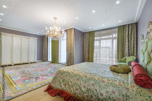 Spacious bedroom in an elegant classic style. Beautiful drapery on the windows, 
a luxurious chandelier, a patterned carpet on the floor.