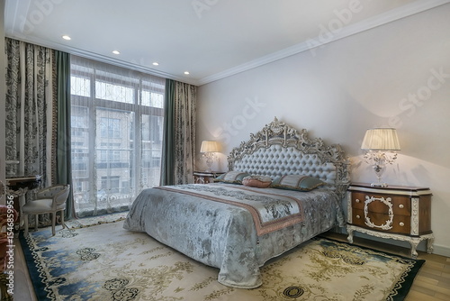 Luxurious bedroom interior in classic style. Beautiful drapery on the window, 
furniture with carvings on curved silver-plated legs, patterned carpet on the floor.