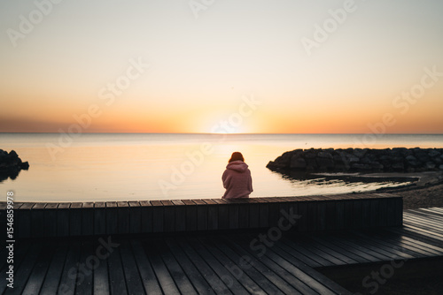 Woman sitting on a bench watching the Sunrise by the Lake Michigan, golden hour, Chicago, Illinois, USA