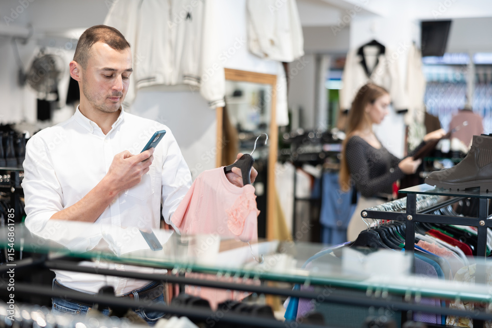 Obraz premium While shopping, man examines womans blouse, photographs product on his phone, shows friend assortment of womens knitwear in video conference mode and advises on choice
