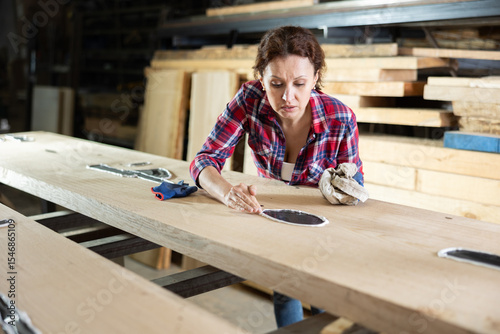 Female sawmill worker cleaning up excess resin or glue on a wooden board