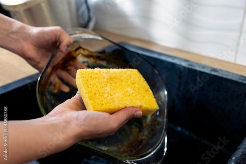 close up girl washing glass baking dish by hand. washing greasy dirty dishes with yellow sponge and detergent