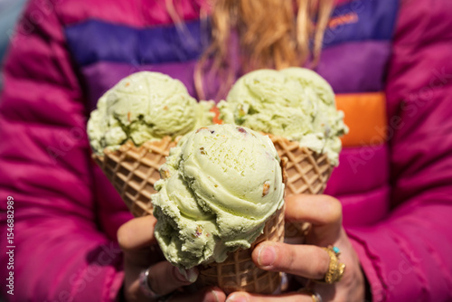 Closeup shot of a woman in a multicolored jacket holding three pistachio ice cream cones