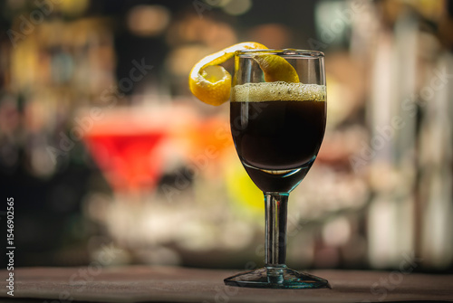 A wine glass, garnished with an orange peel, its dark color betrays a rich and powerful flavor.