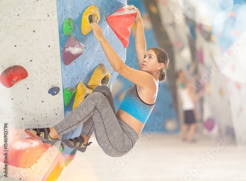 Sportive young girl climbing on artificial rock wall in rock-climbing gym photo