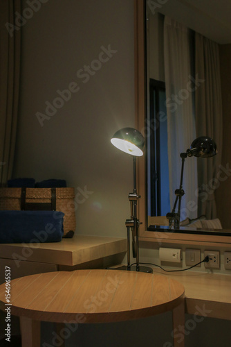 Table lamp on wooden table with mirror in cozy home. Bedside table with night light. Modern creative workspace background