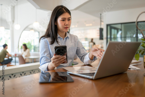 woman is sitting at a table with a laptop and a cell phone