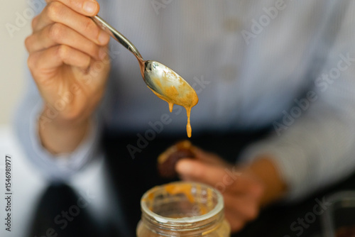 woman's hands holding spoon dripping with peanut butter from the jar