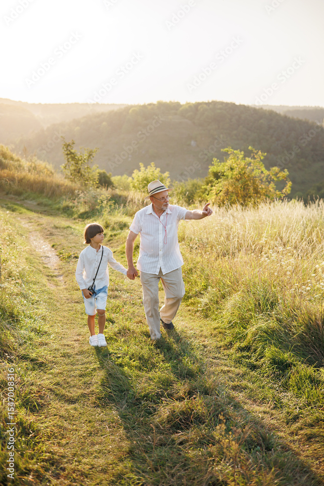 Photo of a little boy with his grandfather walking in a field at summer Photo of a little boy with his grandfather walking in a field at summer