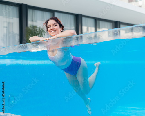 Happy caucasian woman swims in an outdoor pool with a transparent wall in a hotel