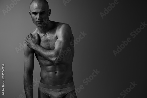 Black and white image of a muscular man posing gracefully, showcasing strong physique and artistry in a dramatic light. Conveying strength and emotion effectively.