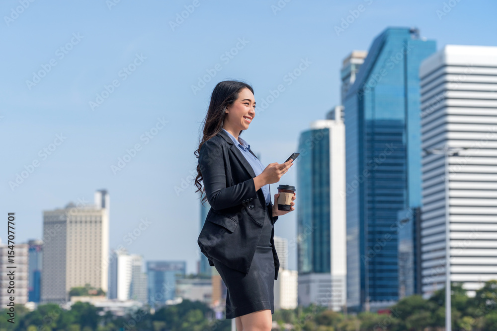 Asian businesswoman using phone in central business district. Businesswoman holding coffee and using smartphone outdoors with modern cityscape background. Asian businesswoman using phone in central business district. Businesswoman holding coffee and using smartphone outdoors with modern cityscape background.