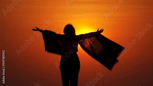 Silhouette of woman with open arms in sunrise against orange sun. Girl enjoying morning sunlight. Carefree person living a free life. Success freedom happy life concept.
