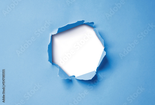 Close-up image of a blue paper sheet with a jagged hole torn through the center, revealing a transparent background.