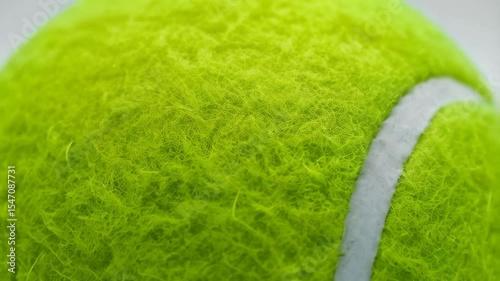 Close-up of a fuzzy bright green tennis ball with a curved white line against a simple, clean white background providing a minimalist and sporty aesthetic.