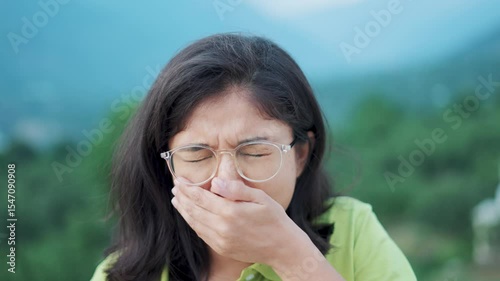 4K shot of Indian teenager girl coughing and covering mouth with hand. Unhealthy sick girl coughing, catching cold, having pneumonia symptoms. Covid pandemic 19, corona virus. 
