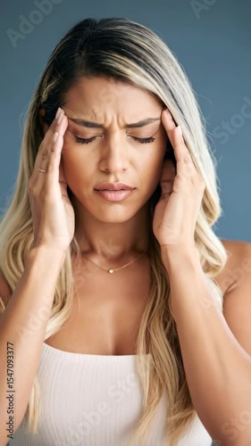 Stressed blond woman massages temples with closed eyes, attempting headache relief in a blue environment.