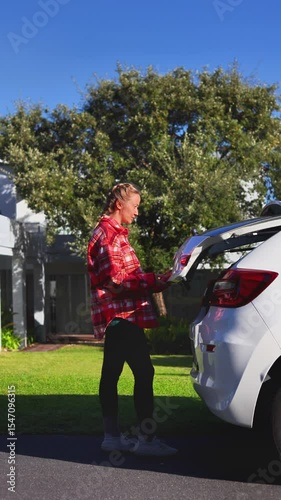 Woman in Plaid Flannel Shirt Unloading Yellow Suitcase from Car Trunk