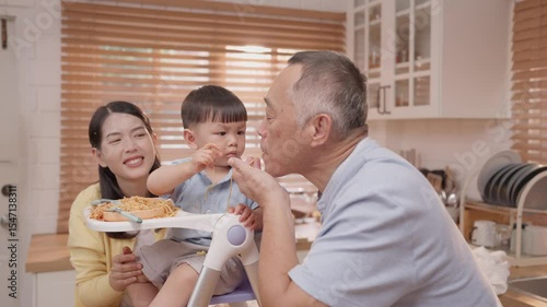 Family enjoys mealtime fun with toddler eating spaghetti in cozy kitchen setting