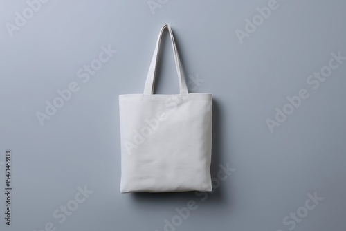 A simple, blank white canvas tote bag hanging vertically against a clean grey background, ready for custom design mockups