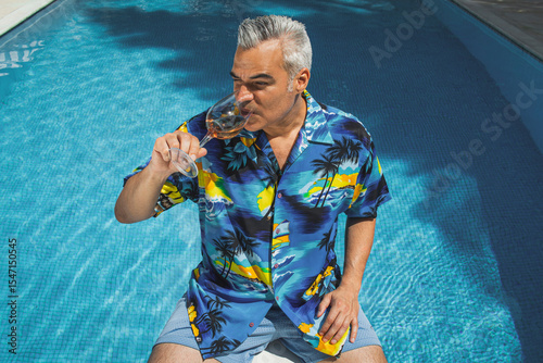 Hispanic mid age Man savoring rose wine by the pool on a sunny day