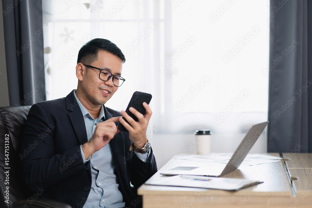 Professional man in suit using smartphone while working at modern desk with laptop and coffee cup in stylish office space with natural light Professional man in suit using smartphone while working at modern desk with laptop and coffee cup in stylish office space with natural light