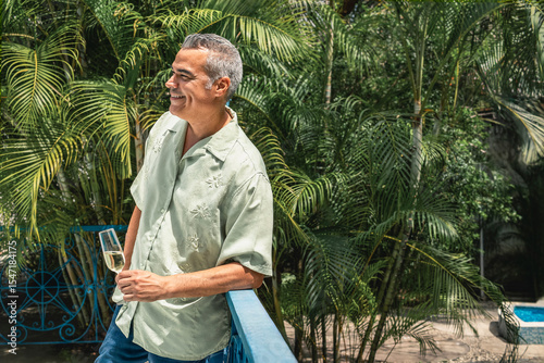 Mature man enjoying a glass of champagne on a tropical balcony