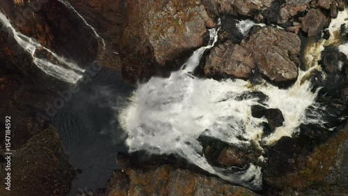 Powerful impact of Voringsfossen waterfall dramatically plunging into deep pool below. Swirling water contrasts sharply with dark rocks in Norway