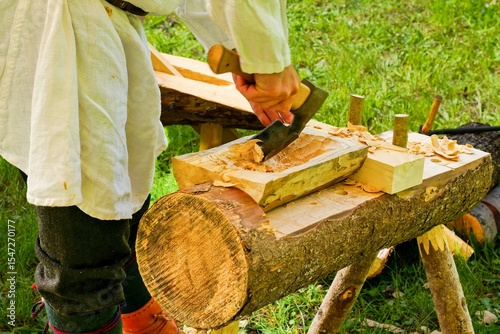 Traditional Woodworking Craftsman Using Axe and Adze. Man in Historical Costume Carving Wooden Log.