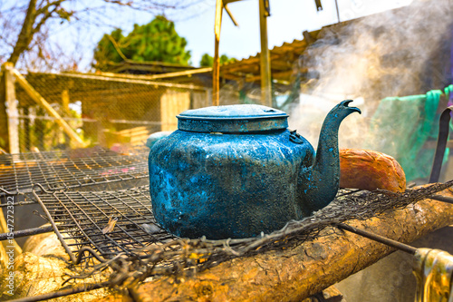 Object Series : Old kettle on charcoal stove. A worn aluminum kettle sits on a metal grate. A kettle that has been used for a long time in the countryside.
