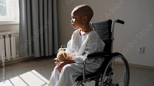 Brave cancer patient young boy in hospital gown sitting alone in wheelchair by window in sunlit hospital room, symbolizing resilience, hope, healthcare, disability, childhood, recovery
