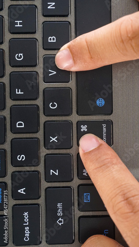 Full frame and close up view of finger pressing command and V or command + V shortcut keys for paste on a wireless computer keyboard