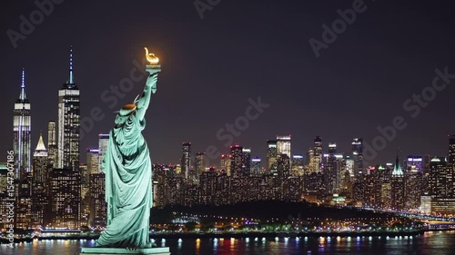Statue of Liberty at night with illuminated New York City skyline in background, symbol of freedom, immigration, democracy, urban life, and iconic American cultural heritage