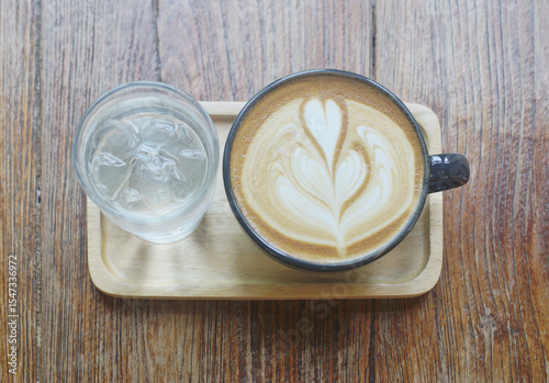 Latte coffee and fresh drinking water on wooden tray