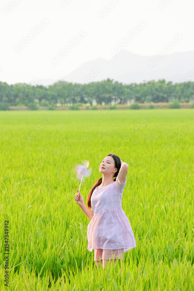 A beautiful Chinese woman playing with a windmill in a rice field during summer A beautiful Chinese woman playing with a windmill in a rice field during summer