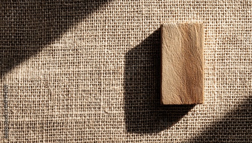 Small wooden rectangle on burlap fabric with sun shadow for texture and contrast, ideal for web banners, advertising designs, and social media content with copy space. 