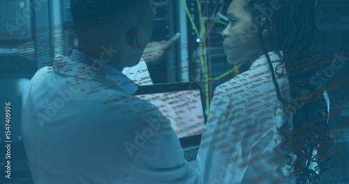 Pointing techs in lab coats examining server racks and Ethernet cables in server room, with laptop
