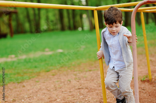young boy at playground playing on jungle gym in casual clothes. kid explores outdoor adventure while enjoying physical activity. green and brown landscape adds natural background.