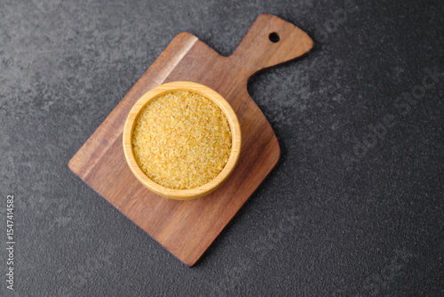 Cracked wheat groats in wooden bowl on black background. Healthy raw cereal grains.