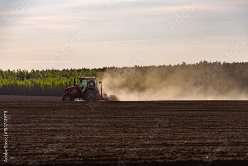 Modern tractor equipment plowing agricultural field or meadow on a farm in spring or autumn during sunset. Farmer cultivating, making soil treatment before sowing plants, crops. photo