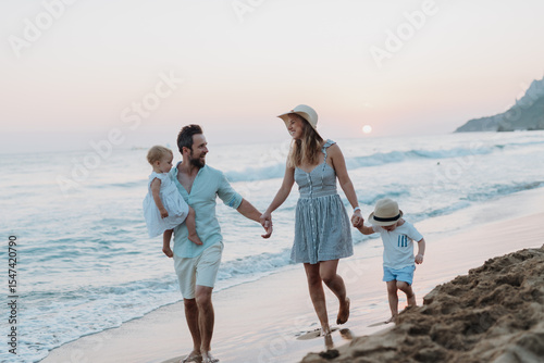 Young family walking on sandy shore during summer beach holiday.