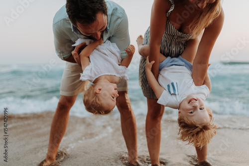 A young family with two toddler children having fun on beach on summer holiday.