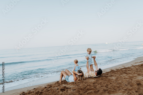 Parents lying in sand and having fun with kids on beach on summer holiday.