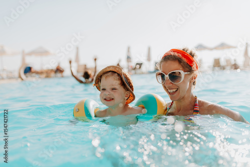 Happy mother swimming with toddler in pool during summer vacation