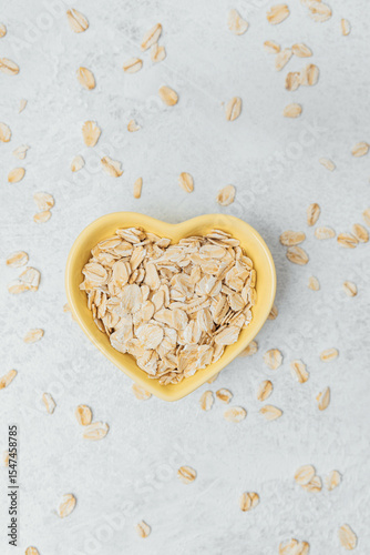 Oats in a heart-shaped bowl surrounded by scattered flakes on a light surface