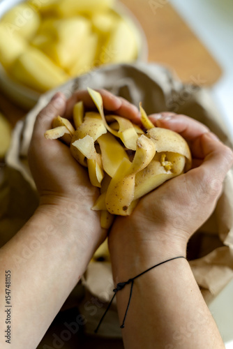 Female hands holding organic potato peelings on blurred background of paper bag for further processing of organic waste. Sorting and recycling of garbage.