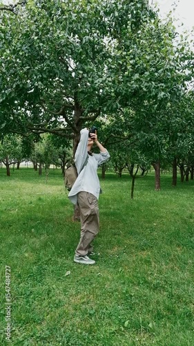 young female photographer taking photos of trees in park bright natural outdoor setting creative nature concept
