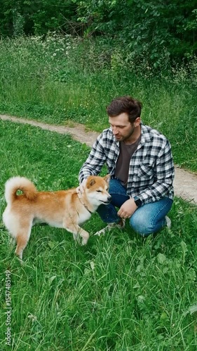 young man in plaid shirt playing training petting hugging and kissing his dog during summer park walk happy loving companionship concept lifestyle	