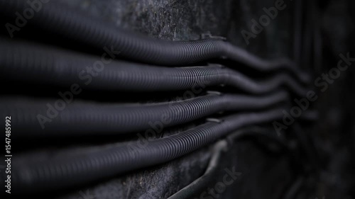 Close-up of long dusty wires in a corrugation stretch along a gray old wall in a subway tunnel. 