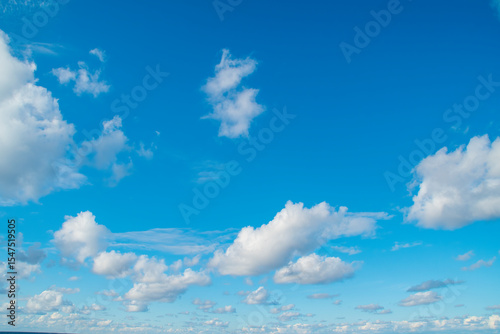 A vast expanse of bright blue sky dotted with fluffy white clouds.Several clouds of varying sizes are scattered across the blue background.This evokes a sense of open space and a peaceful atmosphere